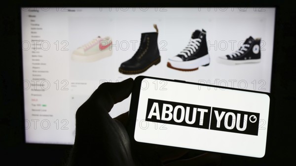 Stuttgart, Germany, 03-14-2023: Person holding cellphone with logo of German e-commerce company About You SE Co. KG on screen in front of webpage. Focus on phone display, Europe