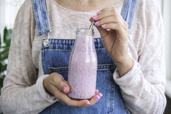 Female hands holding Blueberry smoothie topped with blueberries. Woman eating glass of breakfast protein smoothie drink made from pureed raw blueberries, banana, milk, yogurt, and cottage cheese. Vegetarian vegan food