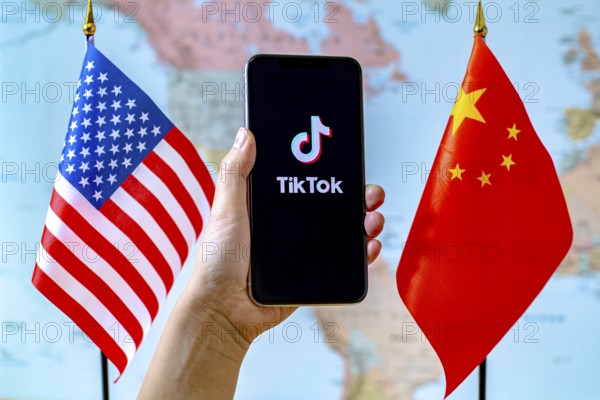 Calgary, Alberta, Canada. Sep 8, 2020. A person holding an iPhone with the TikTok app screen next to a USA and China flags on a world map