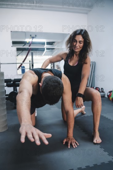 A personal trainer assists a man in a gym during a workout session, tarragona, spain