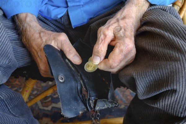 An old man takes a two euro coin from his worn wallet. Close-up, landscape format. An old man takes a two-euro coin out of his worn-out purse. Close up, horizontal format