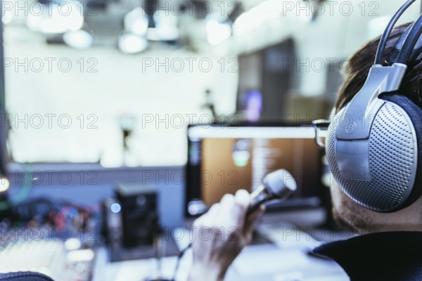 Young man is sitting in the recording studio and talks into the microphone, buttons and equipment in the blurry background