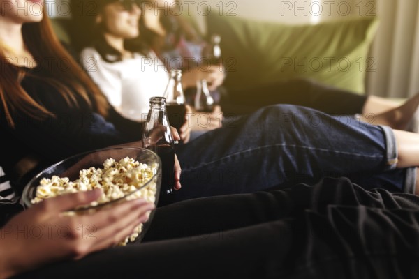 Friend group of people in 3D glasses are watching a movie, smiling, laughing. Eating and drinking while watching a movie in the cinema. Girls eat popcorn and drink soda in glass bottles. Relaxing time