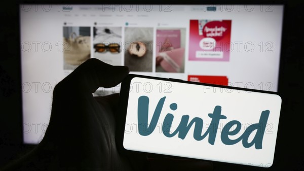 Stuttgart, Germany, 03-17-2024: Person holding mobile phone with logo of online secondhand marketplace company Vinted in front of business web page. Focus on phone display, Europe