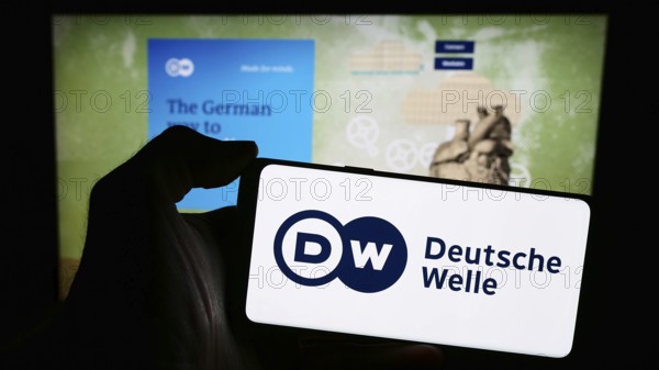 Stuttgart, Germany, 04-10-2024: Person holding mobile phone with logo of German state-owned broadcaster Deutsche Welle (DW) in front of web page. Focus on phone display, Europe