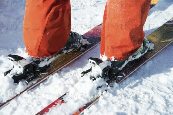 Orange alpine ski boots in a ski mount. One boot is completely fixed on skis, the second is not. Close-up. Orange suit