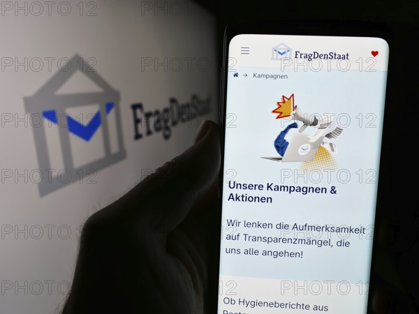 Stuttgart, Germany, 05-21-2024: Person holding smartphone with webpage of German non-governmental organization FragDenStaat in front of logo. Focus on center of phone display, Europe