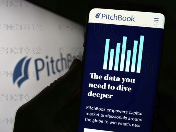 Stuttgart, Germany, 07-26-2023: Person holding cellphone with webpage of US analytics company PitchBook Data Inc. on screen in front of logo. Focus on center of phone display, Europe