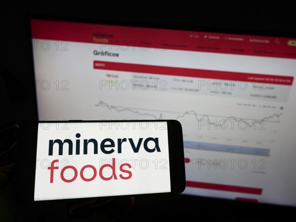 Stuttgart, Germany, 03-30-2022: Person holding mobile phone with logo of Brazilian foods company Minerva SA on screen in front of business web page. Focus on phone display, Europe