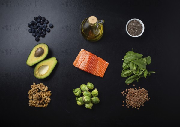 Set of food products as healthy fat sources, ingredients rich in Omega fatty acids: salmon fillet, vegetables, berries, nuts, seeds, olive oil on black chalk board background top view flat lay