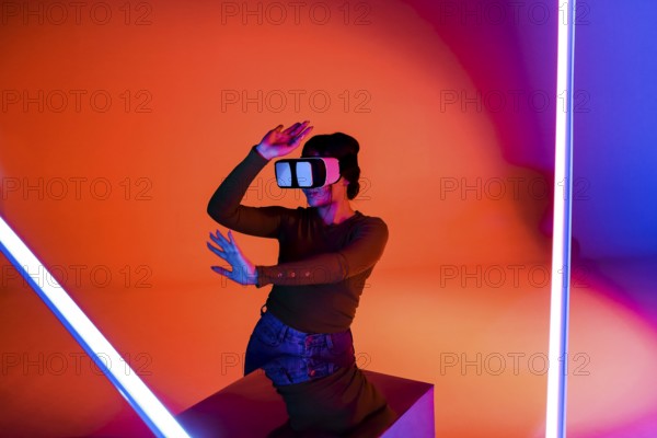 Happy female in VR headset smiling and exploring virtual reality under red neon illumination in futuristic room