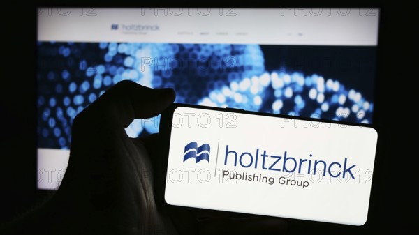 Stuttgart, Germany, 05-22-2024: Person holding mobile phone with logo of German media company Holtzbrinck Publishing Group in front of business web page. Focus on phone display, Europe