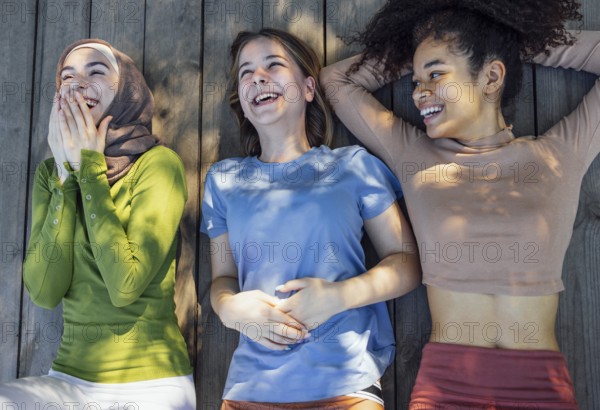 Multiracial young teen female friends resting in the park after sport training laughing and having fun together. Diversity, sport and friendship concept