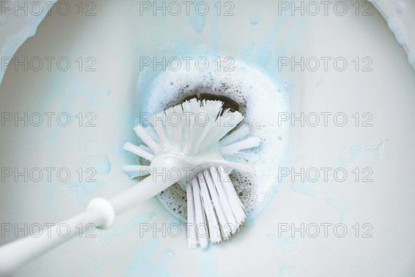 Cleaning a toilet bowl with a brush and strong chemical cleaning foam that pollutes the environment, concept for excessive hygiene versus sustainability household, copy space, selected focus