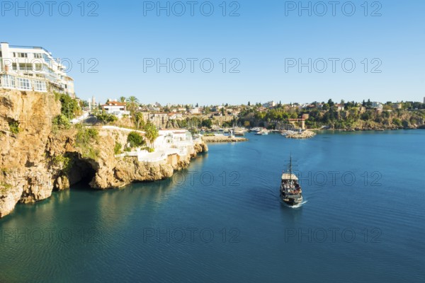 Tourist boat approaches the entrance to sea cave seen from Yavuz Ozcan Park with harbor in background in Antalya, Turkey. Horizontal