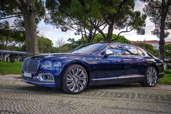 Lisbon, Portugal, Jan 20, 2024: Luxury Bentley Flying Spur Mulliner parked on a cobblestone road, dark blue body and shiny chrome wheels, unique grille and Mulliner make badge, Europe
