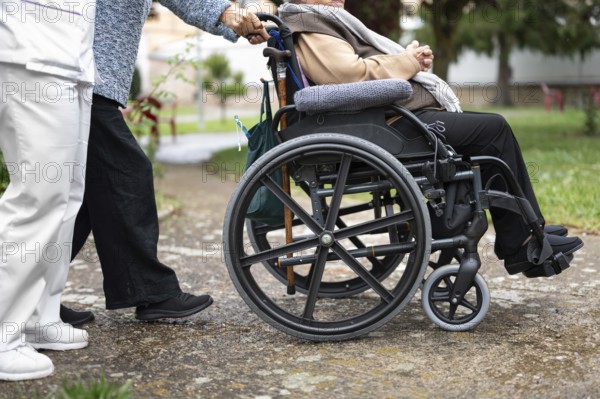 Senior woman in wheel chair with relative and nurse caregiver, outdoors at nursing home garden. graphy
