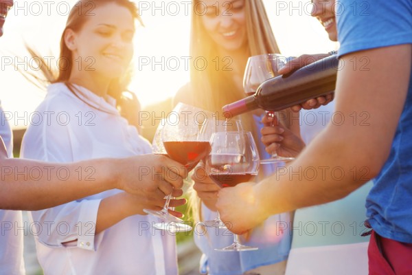 Group of happy friends having red wine on the beach. Sunset beach party