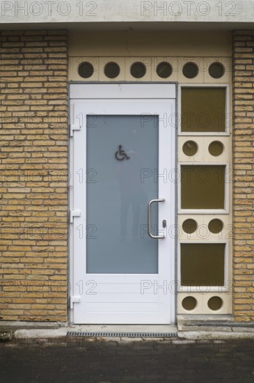 Public restroom door with accessibility sign for disabled people featuring frosted glass and white frame