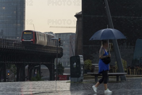 Symbolic picture weather, heavy rain in summer, thunderstorm, storm, tourist with umbrella on the way in the rain next to the underground line U3 at the Landungsbrücken in the harbour of Hamburg, Germany, Europe