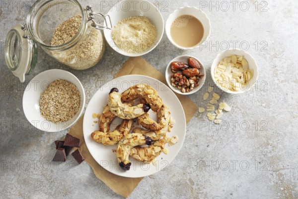 Healthy almond crescent cookies without sugar made from almonds, oat flakes and dates on a plate and ingredient on a rustic gray background, baking at home concept, copy space, high angle view from above