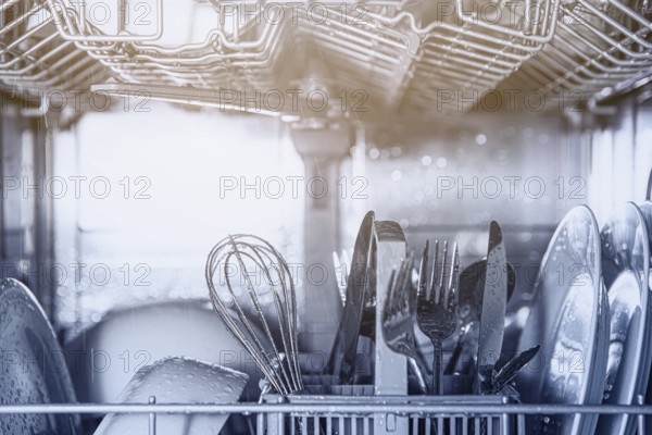 Front view of open automatic stainless steel built-in fully integrated top control dishwasher range machine with clean utensils, cutlery, glasses, dishes, plates inside in modern home kitchen