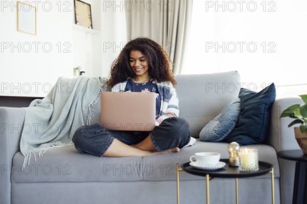 Excited cheerful young black woman using laptop computer on sofa at home, getting good news, feeling joy, doing homework or working online, laughing, happy to win prize