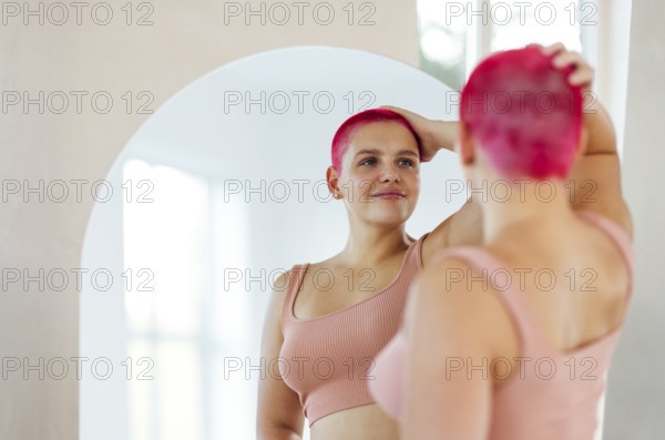 Beautiful relaxed woman in sport clothes red shot hair looking to the mirror. Concept of body positive