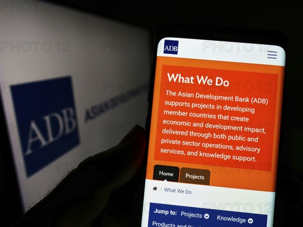 Stuttgart, Germany, 08-28-2022: Person holding cellphone with webpage of organization Asian Development Bank (ADB) on screen in front of logo. Focus on center of phone display, Europe
