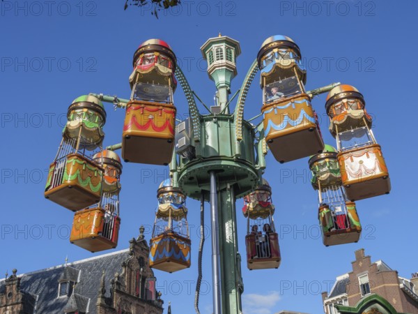 Colourful carousel cabins in an amusement park in front of historic buildings under a clear sky, joyful atmosphere, nijmegen, the netherlands