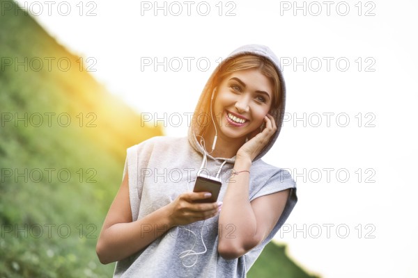 Beautiful young woman with headphones glad after nice jogging in city park