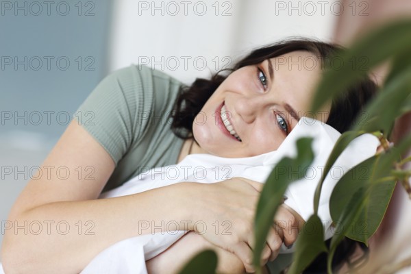 Happy cheerful young woman with big blue eyes resting relaxing at home on weekend, enjoying leisure time indoors, looking with bright toothy smile at camera against apartment indoor interior