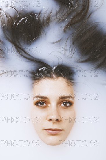 beauty portrait of young woman face and brunette long hair floating in milk bath