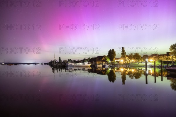 Colourful northern lights reflected in a quiet night lake next to illuminated buildings, harbour, Allensbach, Lake Constance, Baden-Württemberg, Germany, Europe