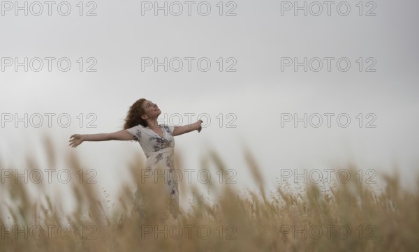 Happy woman in a floral dress stands amidst golden wheat, enjoying the serene landscape