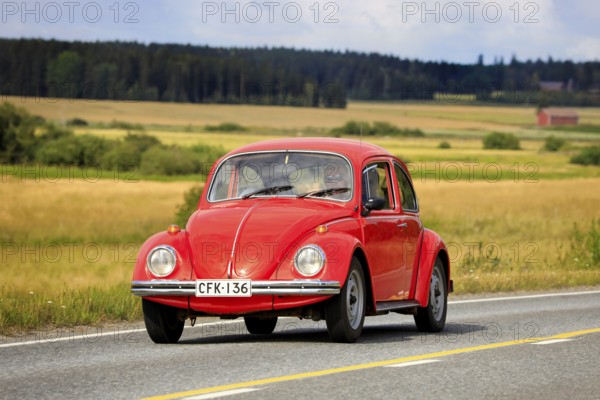 Red Volkswagen Beetle, officially Volkswagen Type 1, driving along country road on Maisemaruise 2019 car cruise. Vaulammi, Finland. August 3, 2019