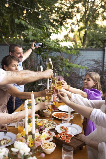 HAppy friends saying cheers and showing their champagne glasses full of sparkling wine to each other whilst enjoying an outdoor wedding party on a backyard restaurant at sunset