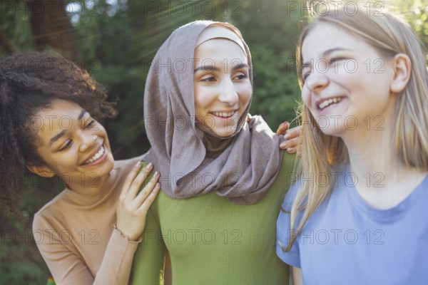 Multiracial young teen female friends walking in the park laughing and having fun together. Diversity and friendship concept
