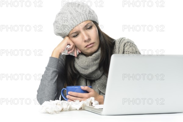 Close up Tired Sick Woman in Gray Winter Attire Working with Her Laptop While Having Cup of hot tea on Desk, isolated on White Background