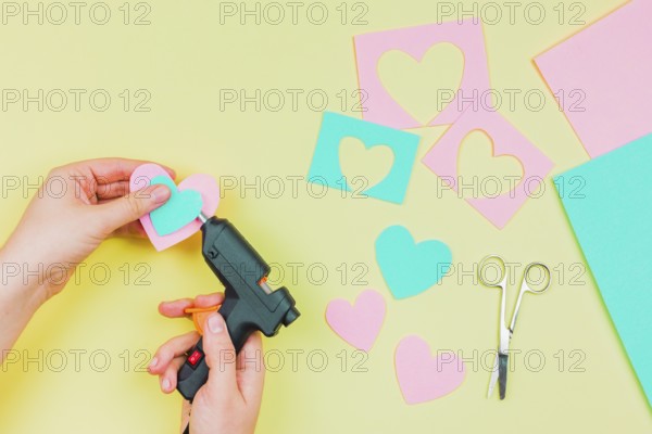 Close up woman s hand sticking paper heart shape with electric hot glue gun