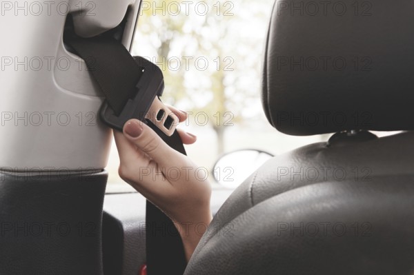 A woman's hand reaches behind her seat belt to fasten it. The concept of safe driving of women by car