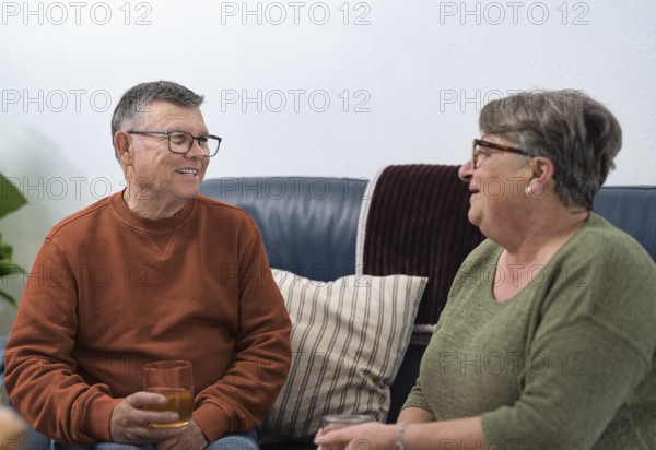 Happy retired couple enjoying a relaxing afternoon at home, sharing stories and drinks on a comfortable sofa, representing a healthy and fulfilling retirement