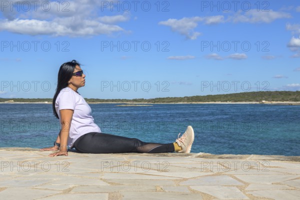 Woman sitting by the ocean, wearing sunglasses, beautiful latina woman by the sea in Colonia San Jordi, Balearic Islands, Majorca, Spain, Europe