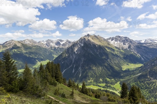 Panorama of impressive, snow-covered Alpine mountains, above a green valley under sun and clouds in Kleinwalsertal, Austria, Europe