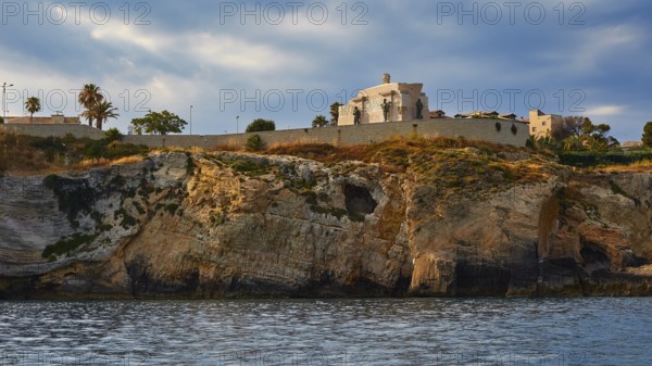 Building on a cliff under a cloudy sky next to the sea, boat trip around the island of Ortigia, Isola di Ortigia, Syracuse, Sicily, Italy, Europe