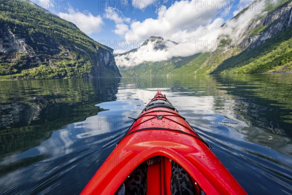 Kayak trip on the Geirangerfjord, tip of a red kayak in the fjord with reflection, atmospheric fjord landscape, first person view at Geiranger, Møre og Romsdal, Norway, Europe