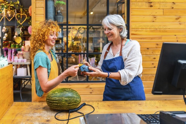 Happy customer paying with contactless credit card for a melon at a flower shop counter, small business and electronic payment concept