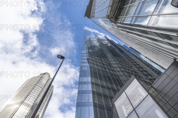 Low angle view of modern skyscrapers in london's financial district, showcasing their towering presence against a blue sky with clouds