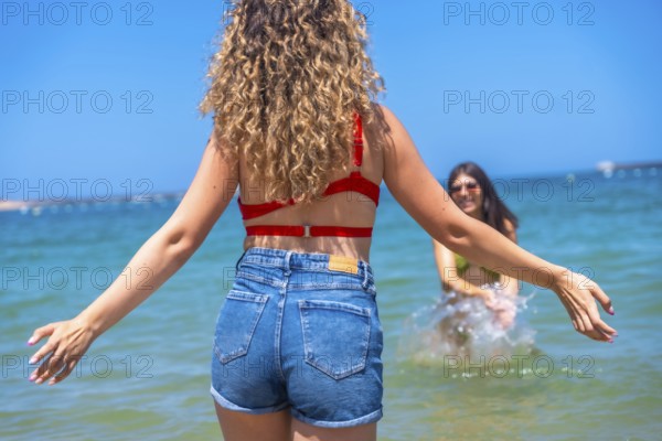 Two young women are enjoying their summer vacation, playing and splashing in the refreshing ocean water under a clear blue sky