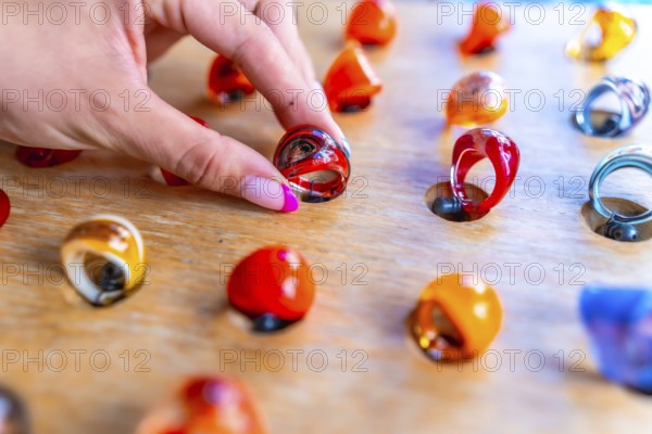 Woman's hand with pink nail polish picking up a colorful resin ring from a wooden display at a craft market
